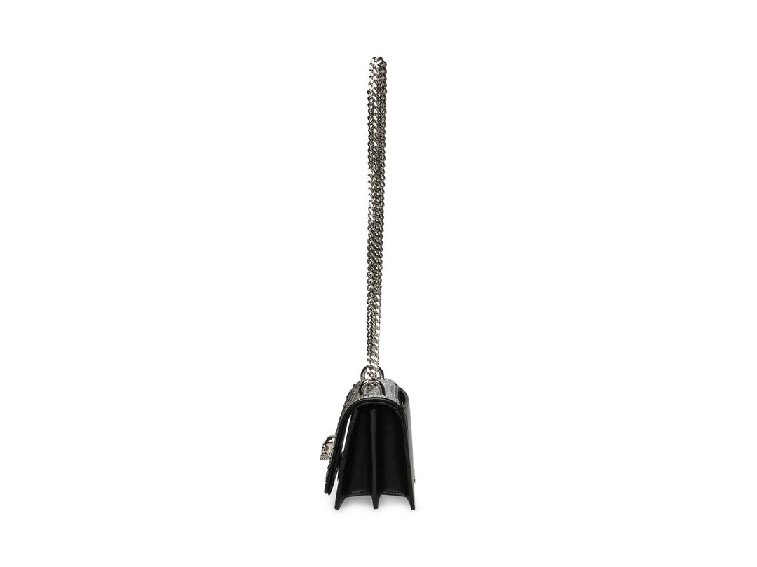 Bolso negro de Steve Madden con cadena plateada, detalles de pedrería brillante y un adorno metálico en forma de ave.