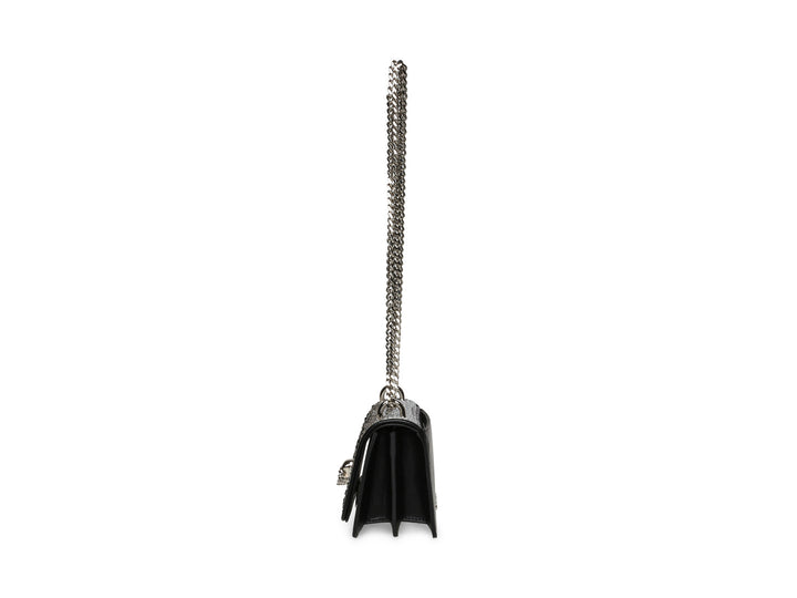 Bolso negro de Steve Madden con cadena plateada, detalles de pedrería brillante y un adorno metálico en forma de ave.