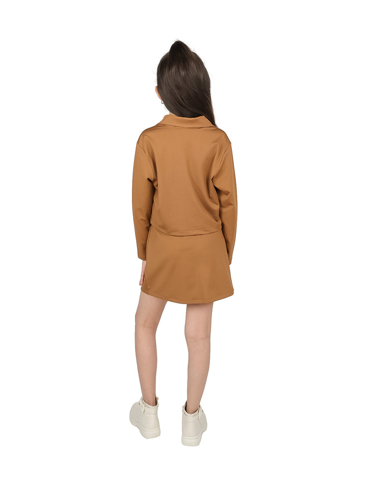 Niña vistiendo un conjunto de chaqueta y falda color café con botas blancas sobre fondo blanco.