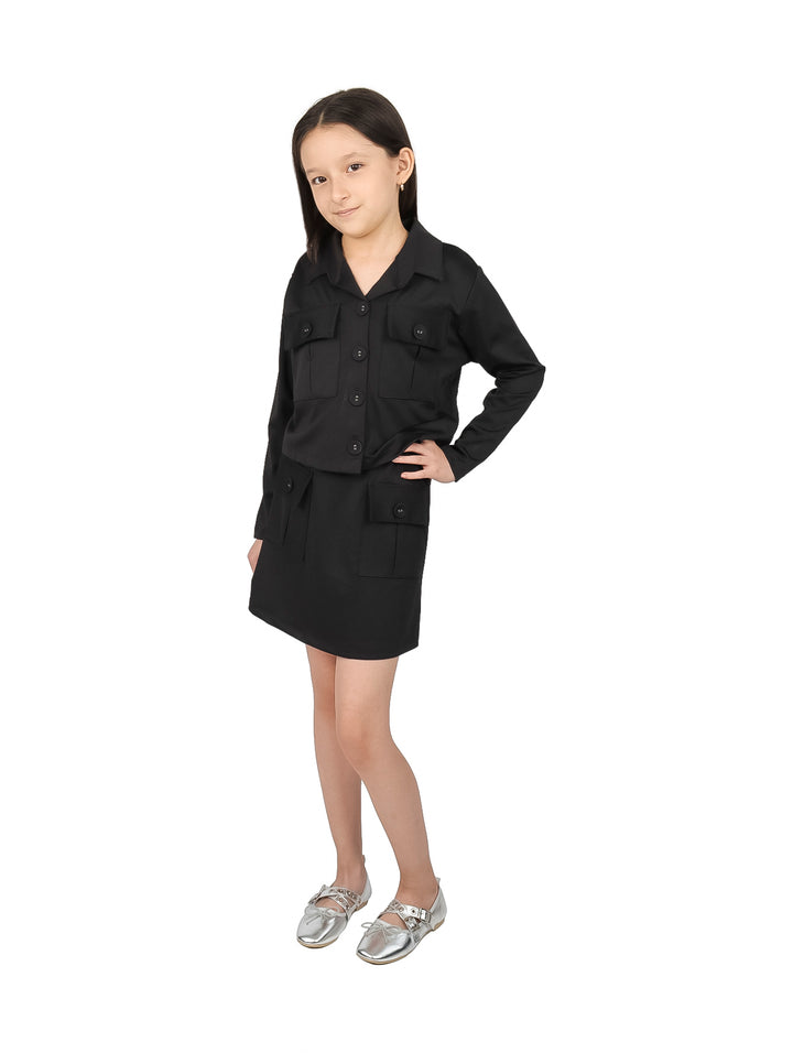 Niña vistiendo un conjunto elegante de chaqueta y falda en color negro con zapatos plateados.