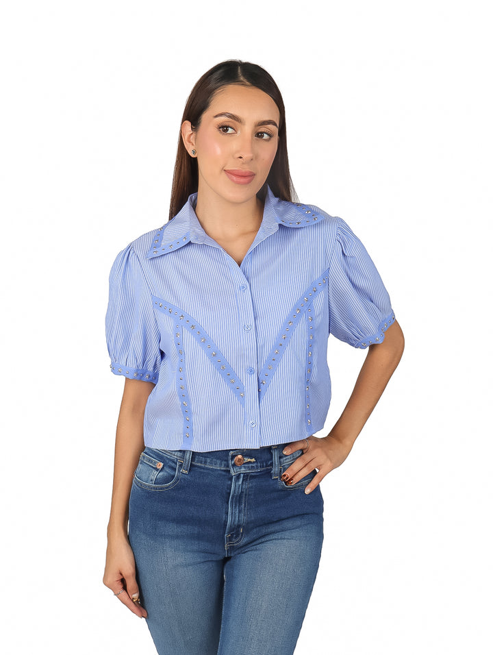 Mujer vistiendo camisa azul y blanca a rayas con detalles metálicos en V y mangas cortas.