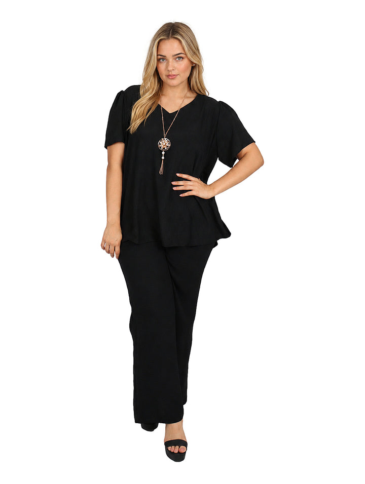 Mujer vistiendo blusa negra de manga corta y cuello redondo con un collar dorado largo decorativo.
