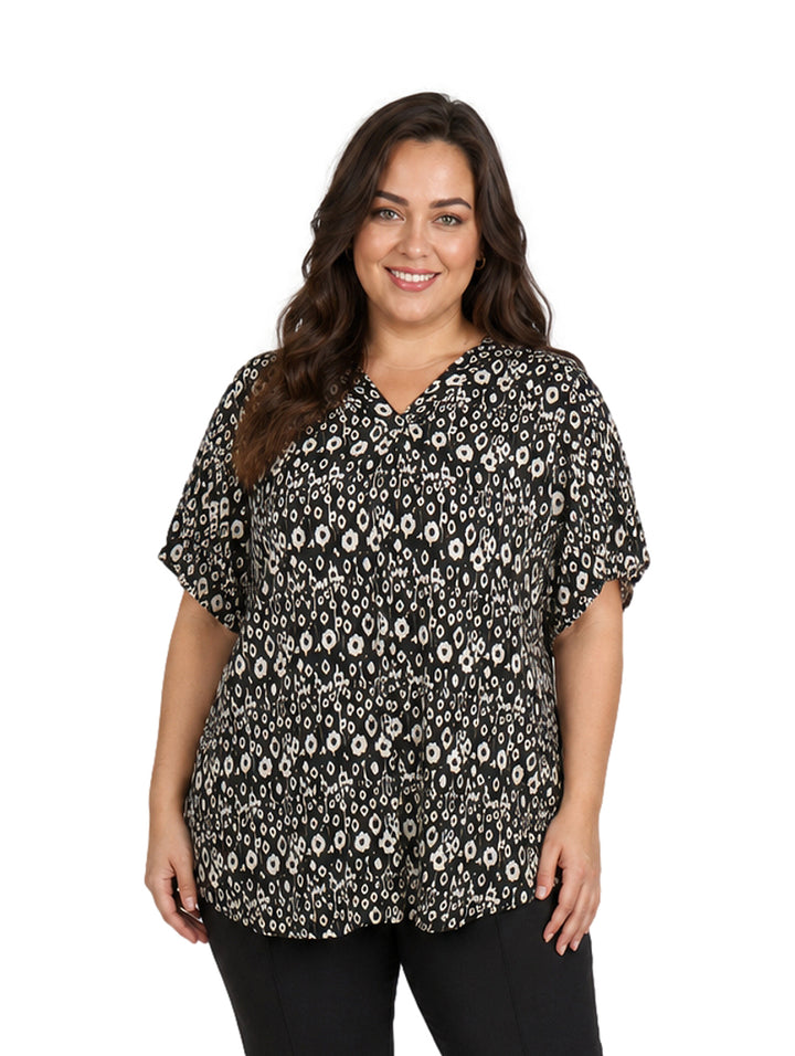 Mujer vistiendo blusa negra con estampado de flores blancas, cuello en V y manga corta.