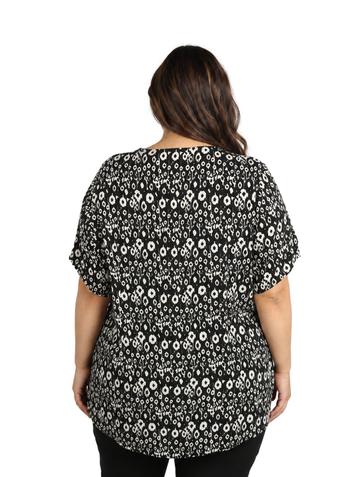 Mujer vistiendo blusa negra con estampado de flores blancas, cuello en V y manga corta.