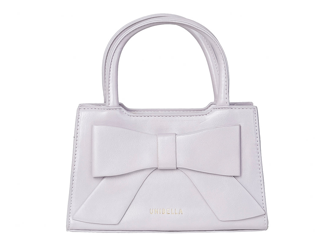Bolso de mano color morado claro con un moño decorativo grande en la parte frontal y asas cortas.