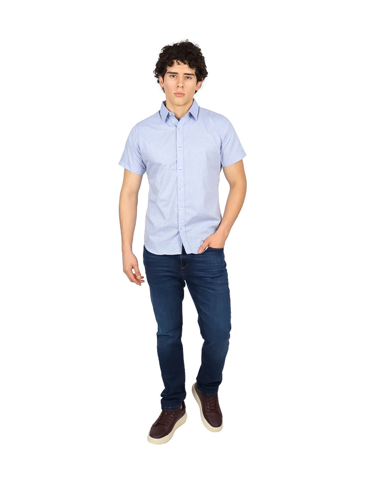 Hombre vistiendo una camisa de manga corta color azul cielo y pantalones vaqueros.