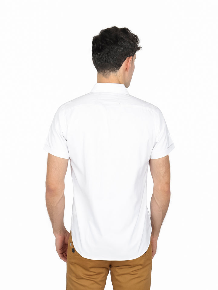 Hombre vistiendo una camisa blanca de manga corta y cuello, combinada con pantalones color café.