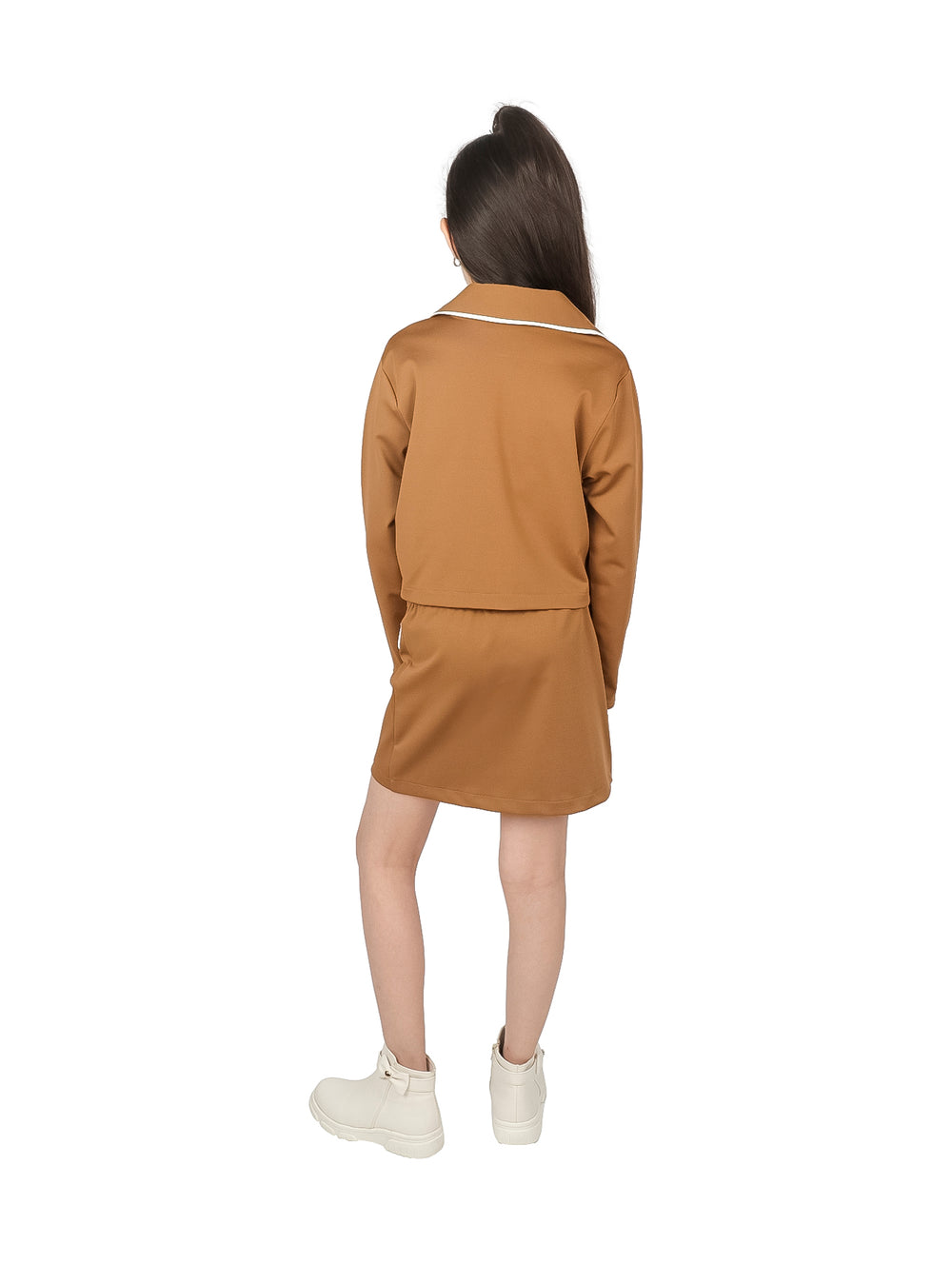 Niña con conjunto de chaqueta y falda color moka con ribetes blancos y botas blancas.
