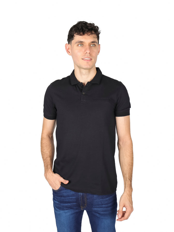 Hombre vistiendo una playera polo de color negro de manga corta y jeans azules sobre fondo blanco.