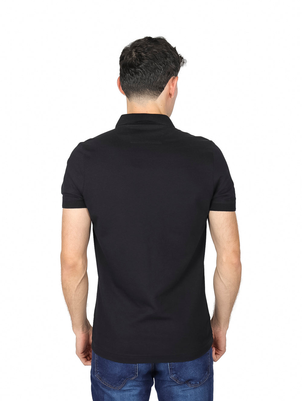 Hombre vistiendo una playera polo de color negro de manga corta y jeans azules sobre fondo blanco.