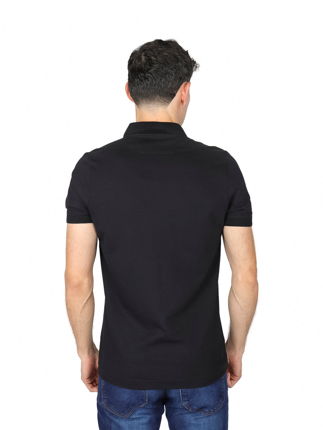 Hombre vistiendo una playera polo de color negro de manga corta y jeans azules sobre fondo blanco.