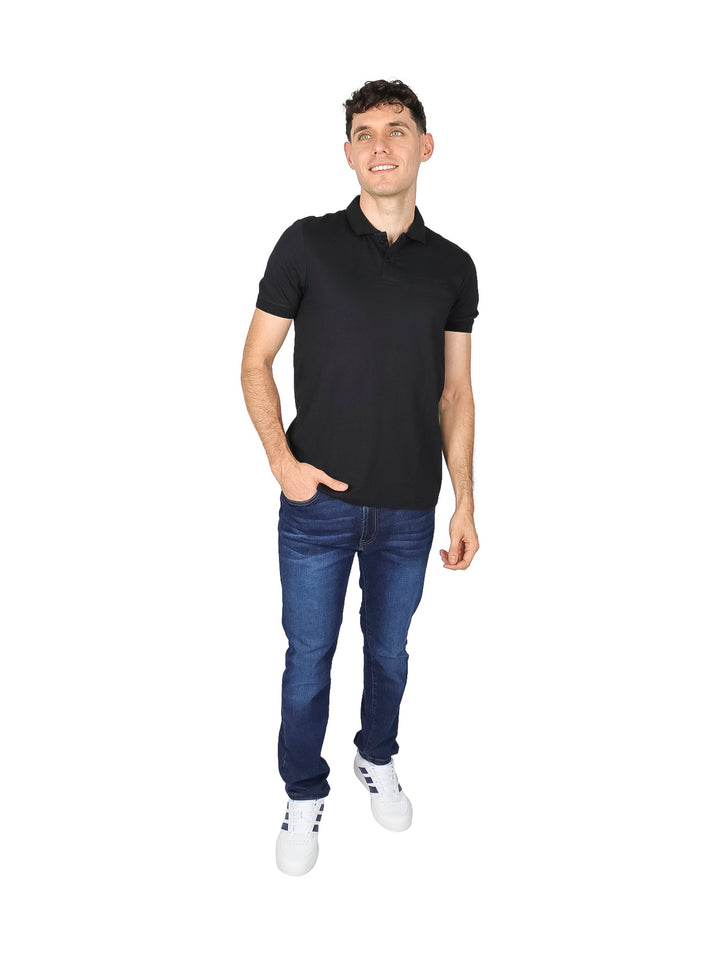 Hombre vistiendo una playera polo de color negro de manga corta y jeans azules sobre fondo blanco.