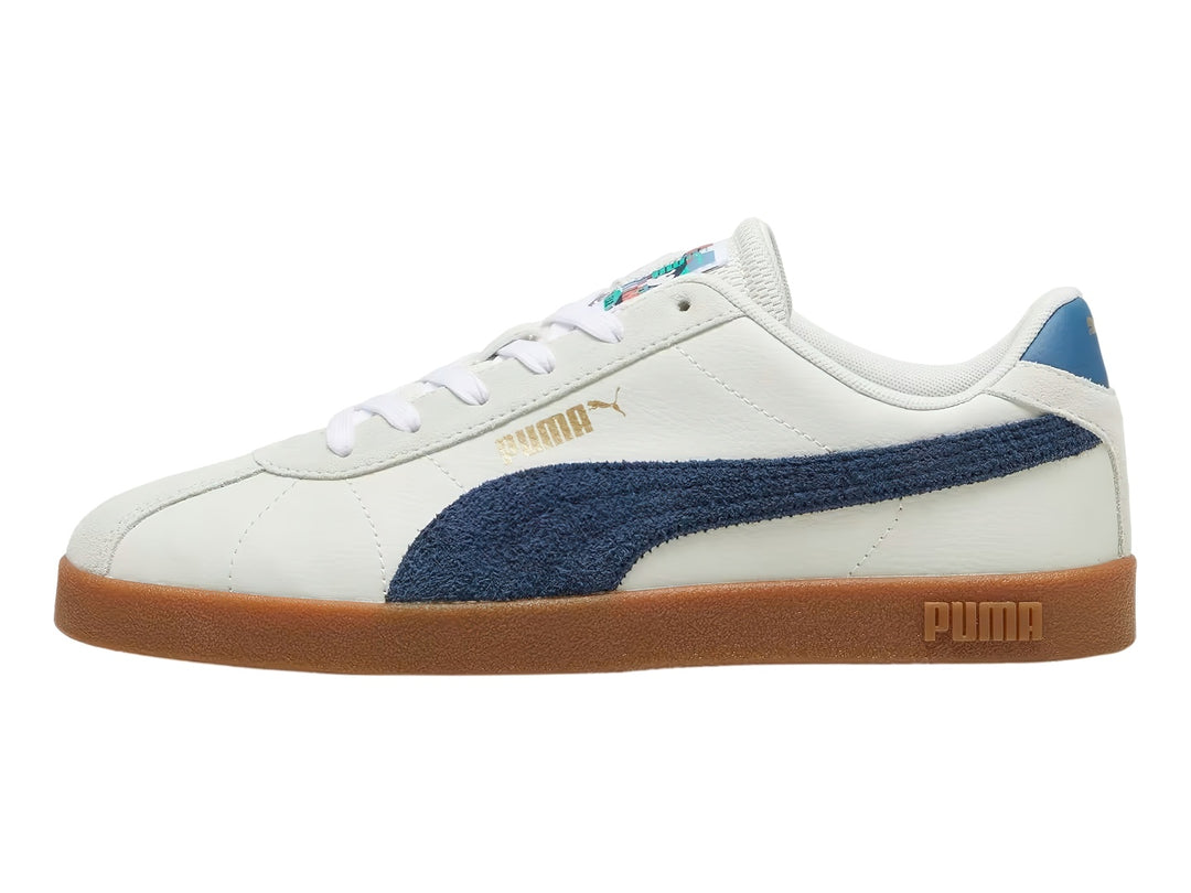 Tenis PUMA blancos con franja azul marino y suela de goma color café.