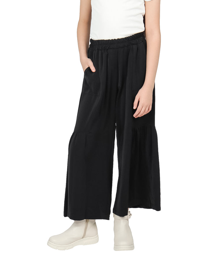 Niña vistiendo pantalón negro de pierna ancha con cintura elástica y botas blancas.