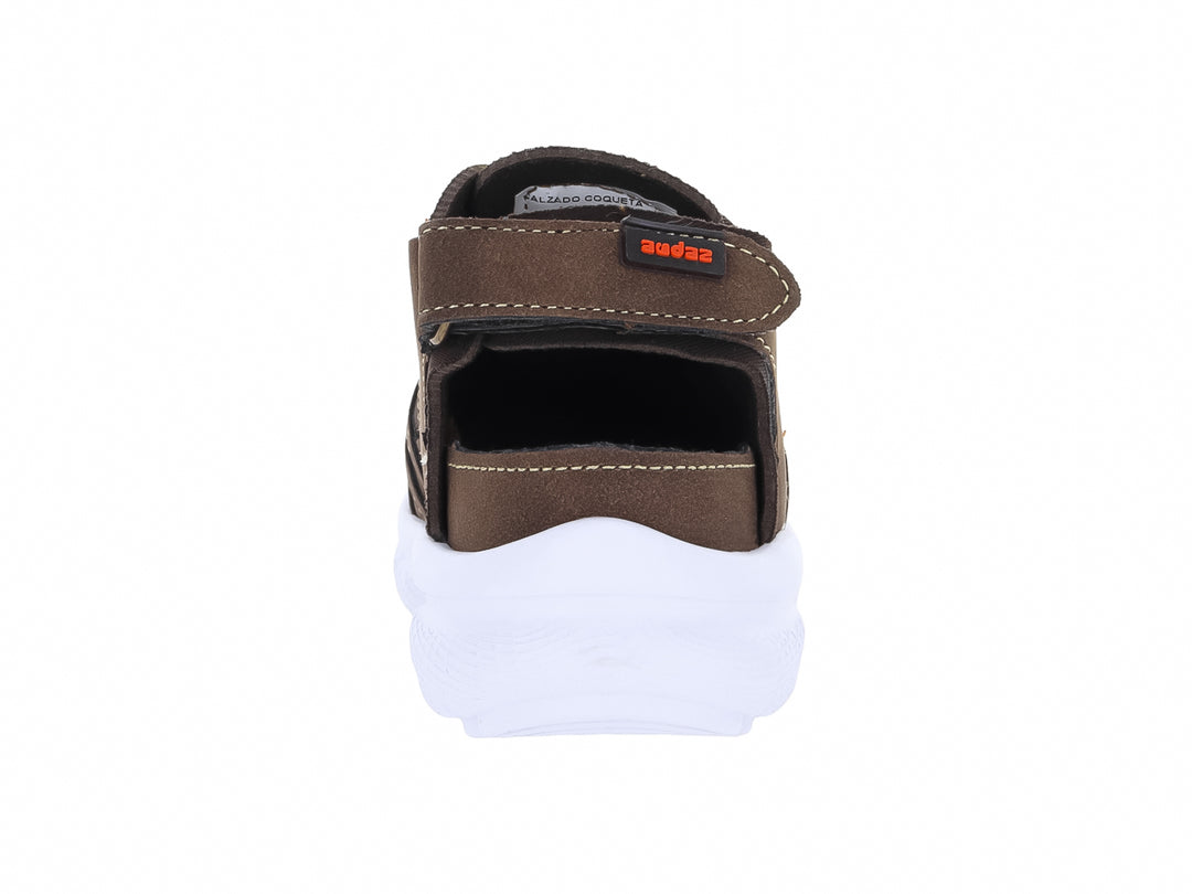 Sandalias cerradas para niña en color café con detalles naranja y suela blanca gruesa.