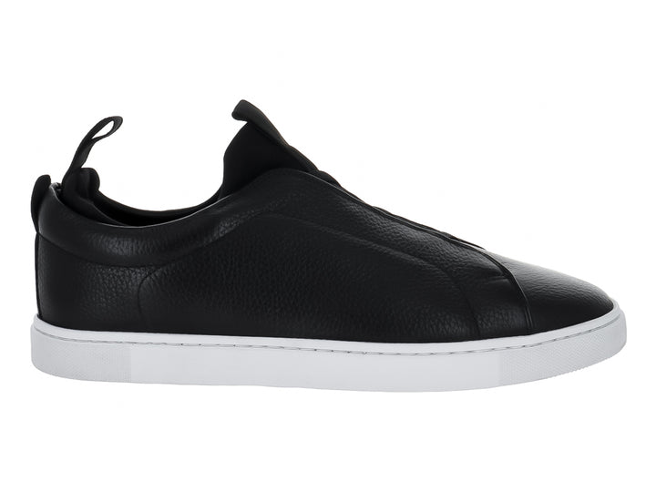 Zapato tipo slip-on de piel negra con suela blanca y pestaña trasera para calce fácil.