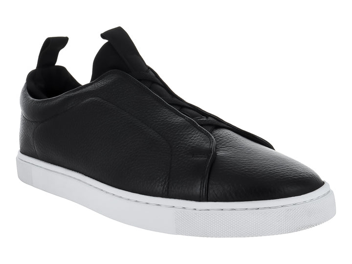 Zapato tipo slip-on de piel negra con suela blanca y pestaña trasera para calce fácil.