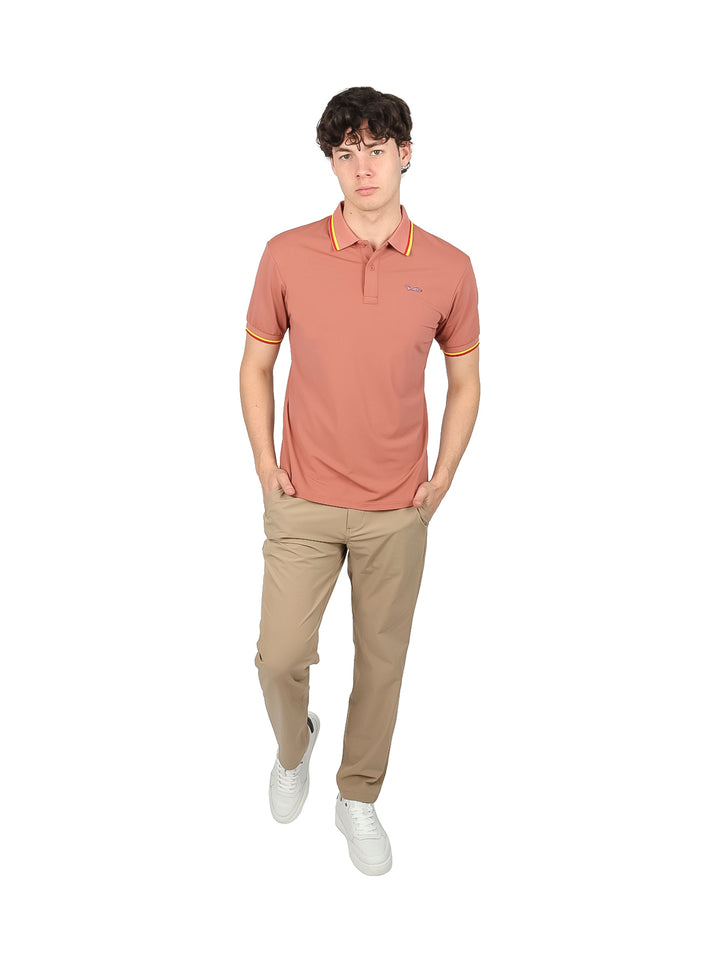 Hombre vistiendo playera polo color marrón con detalles amarillos y rojos en el cuello y mangas.
