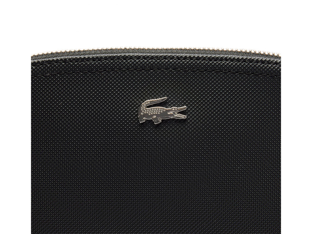 Bolso pequeño de color negro con textura granulada y logotipo metálico de Lacoste en el centro.