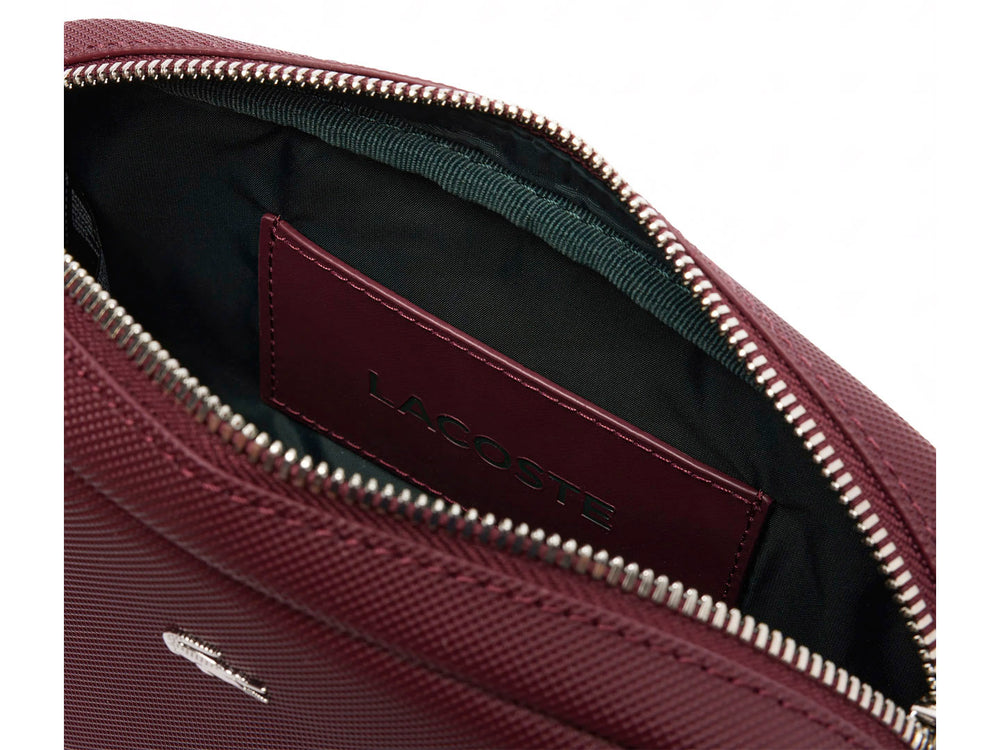 Bolso bandolera Lacoste color tinto con textura granulada, cierre superior y correa ajustable.