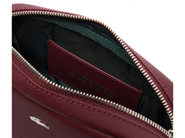 Bolso bandolera Lacoste color tinto con textura granulada, cierre superior y correa ajustable.