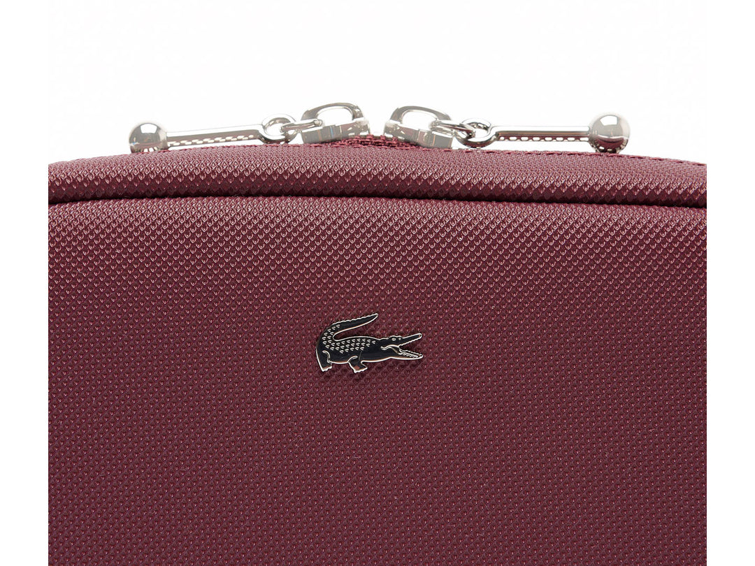 Bolso bandolera Lacoste color tinto con textura granulada, cierre superior y correa ajustable.