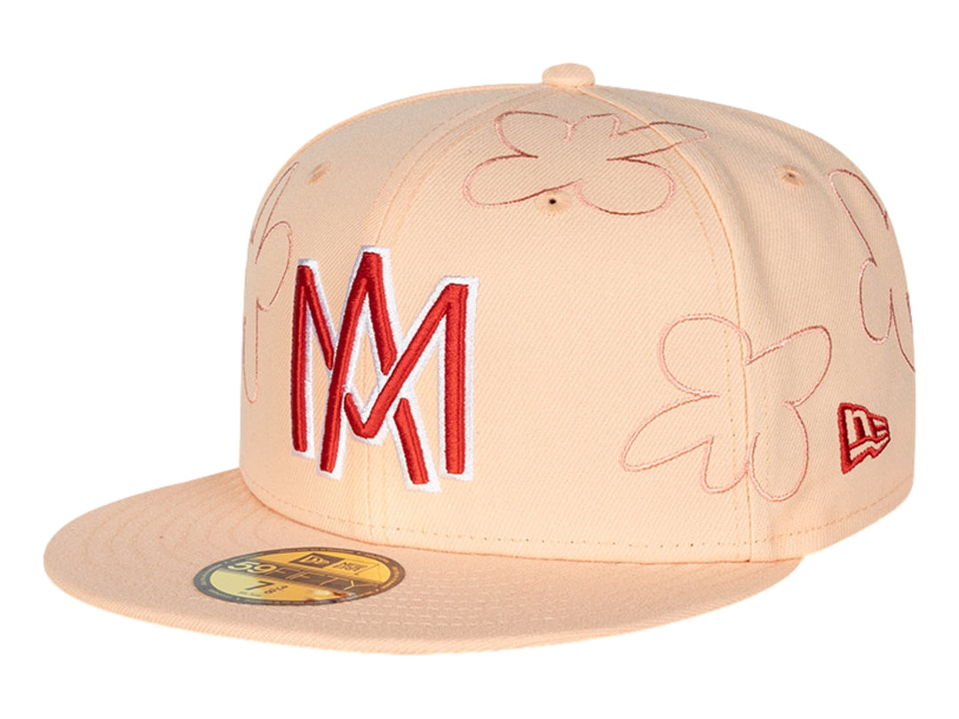 Gorra New Era color rosa con visera plana, bordados de flores y letras 'M' en rojo y blanco.