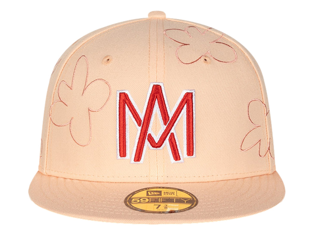 Gorra New Era color rosa con visera plana, bordados de flores y letras 'M' en rojo y blanco.