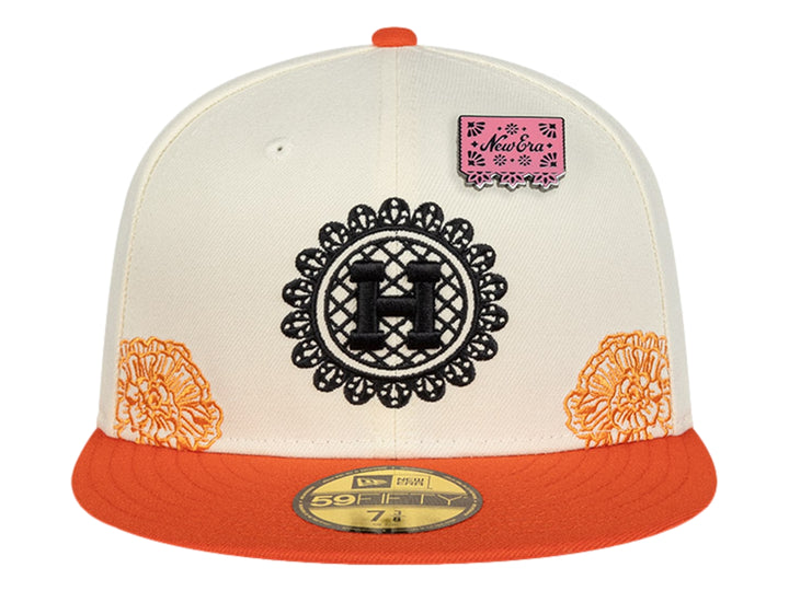 Gorra New Era blanca con visera naranja y detalles de parches y bordados decorativos.