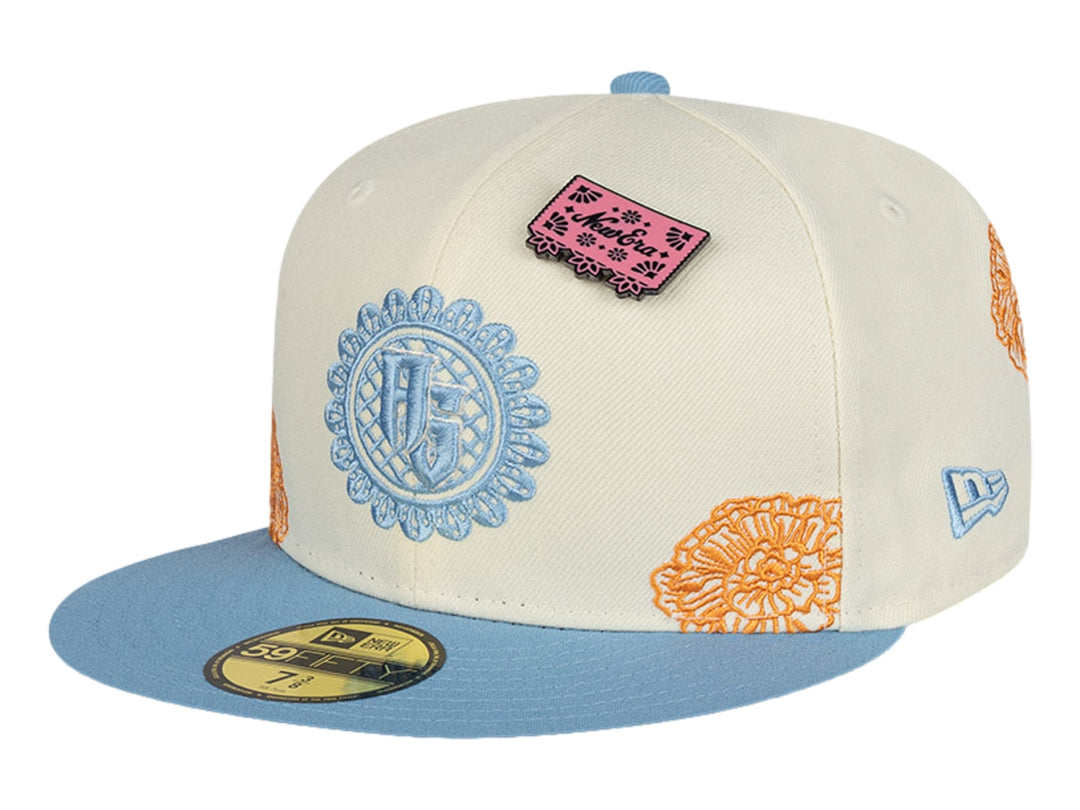 Gorra New Era blanca con visera azul, detalles bordados en naranja y azul, y un pequeño parche rosa.