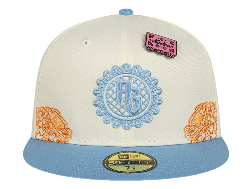 Gorra New Era blanca con visera azul, detalles bordados en naranja y azul, y un pequeño parche rosa.