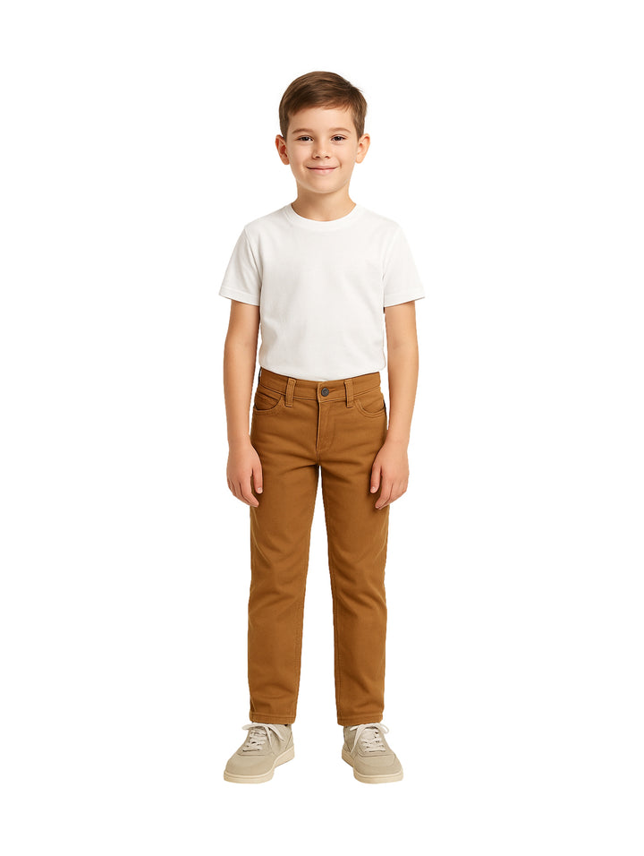 Niño modelando un pantalón casual color tabaco con camiseta blanca y tenis beige.