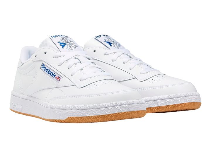 Tenis Reebok Club C 85 blancos con suela de goma marrón y detalles en azul.