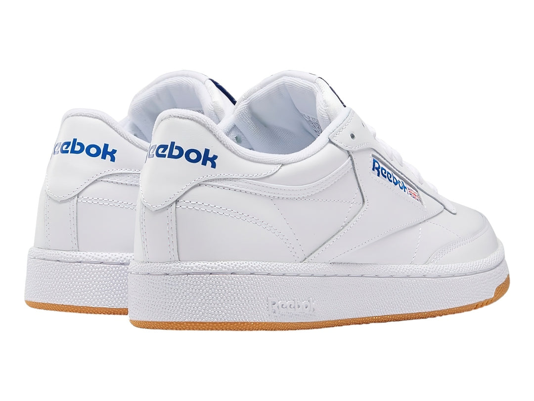 Tenis Reebok Club C 85 blancos con suela de goma marrón y detalles en azul.