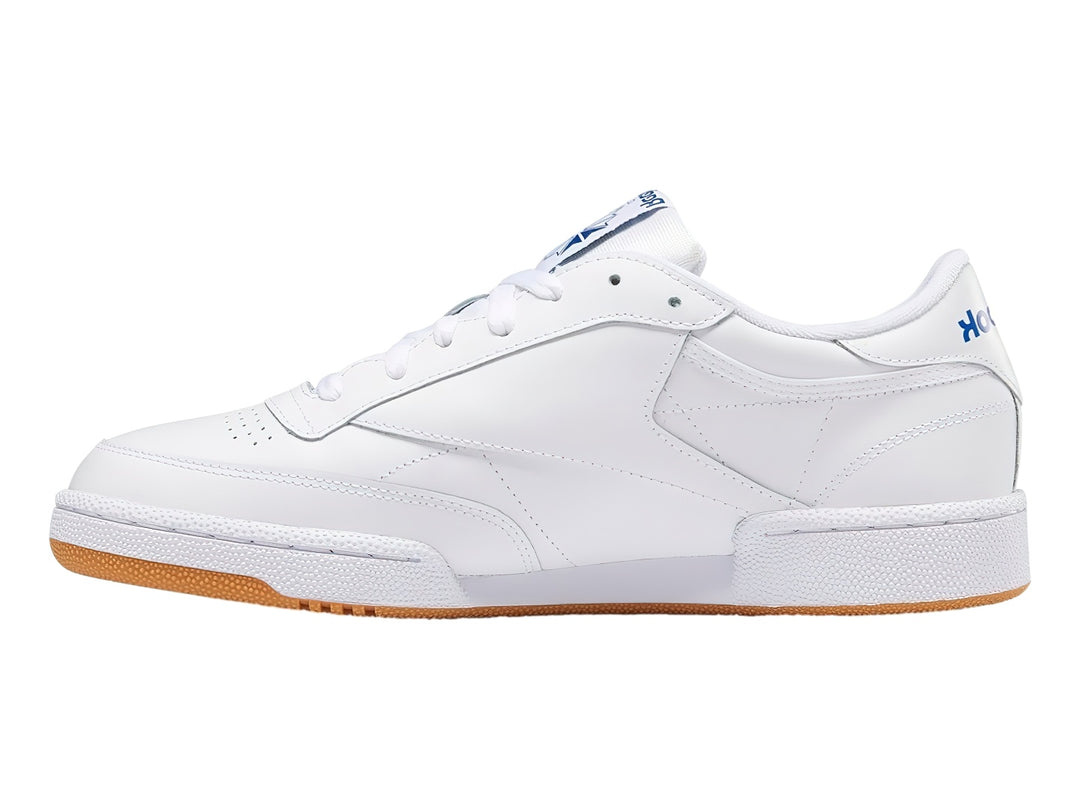 Tenis Reebok Club C 85 blancos con suela de goma marrón y detalles en azul.