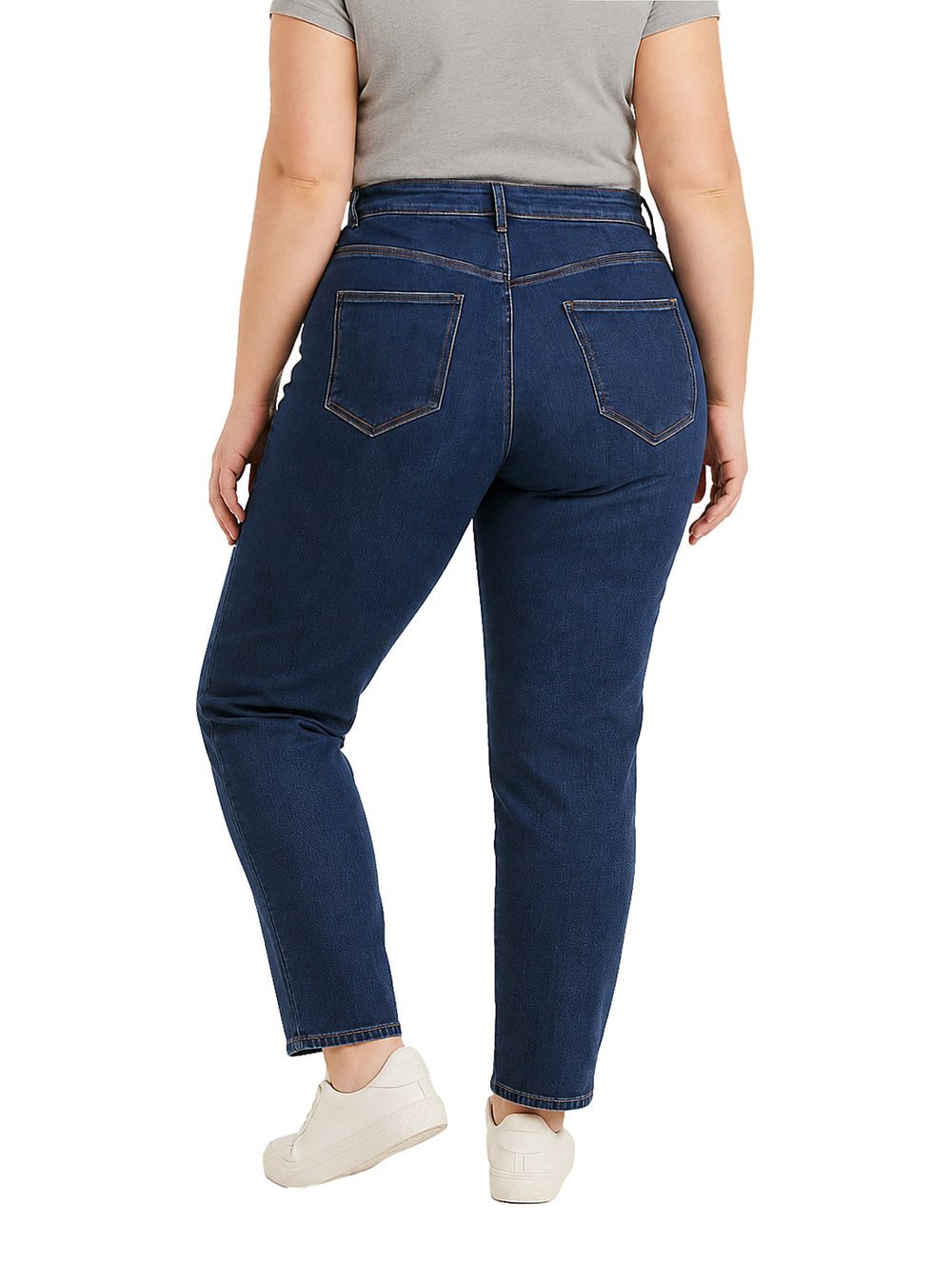 Mujer vistiendo pantalones jeans skinny de color azul oscuro con costuras doradas y tenis blancos.