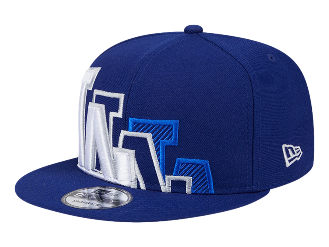 Gorra New Era azul con visera plana y diseño gráfico bordado en blanco y azul en el frente.