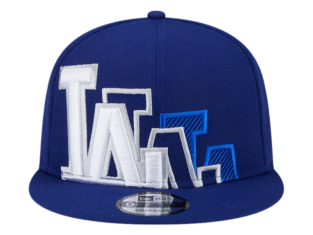 Gorra New Era azul con visera plana y diseño gráfico bordado en blanco y azul en el frente.
