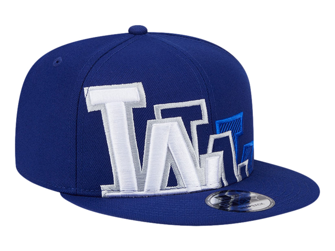 Gorra New Era azul con visera plana y diseño gráfico bordado en blanco y azul en el frente.