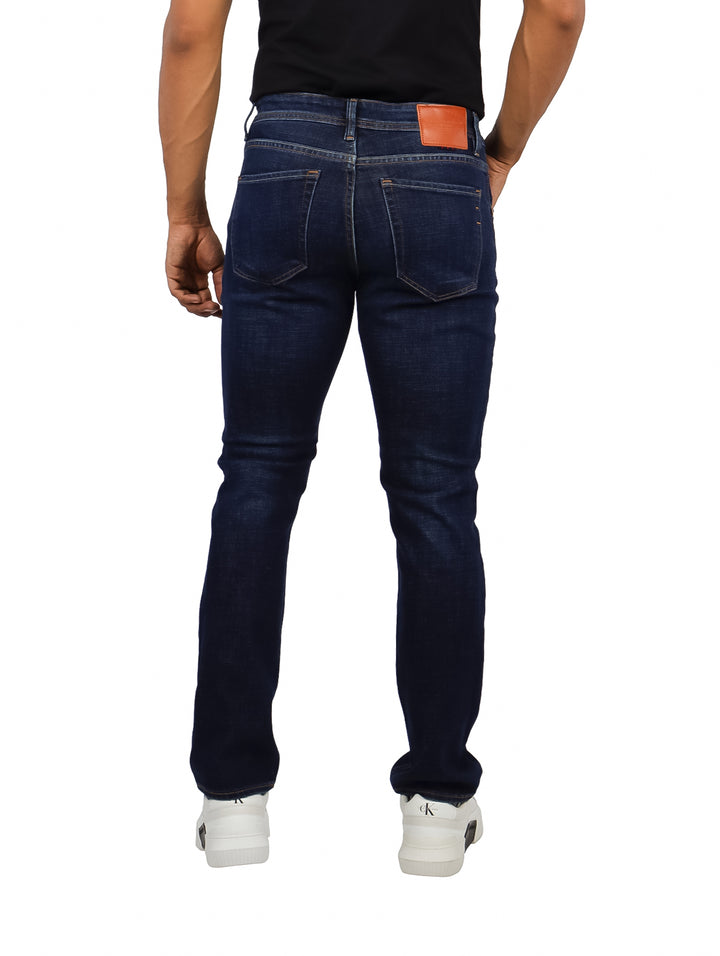 Hombre vistiendo jeans color dark indigo de corte ajustado y tenis blancos.
