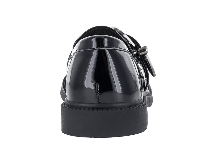 Zapato tipo mocasín para niño en color negro brillante con hebilla decorativa plateada.