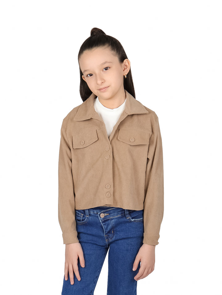 Niña vistiendo chaqueta corta color camel de pana con botones y pantalones azules.