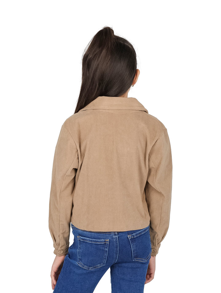 Niña vistiendo chaqueta corta color camel de pana con botones y pantalones azules.