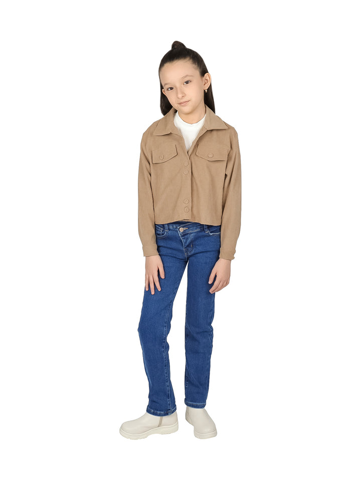 Niña vistiendo chaqueta corta color camel de pana con botones y pantalones azules.