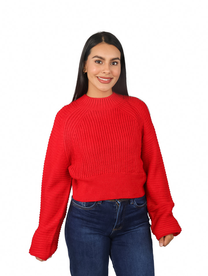 Mujer vistiendo un suéter rojo de tejido acanalado con mangas anchas y pantalones azules.