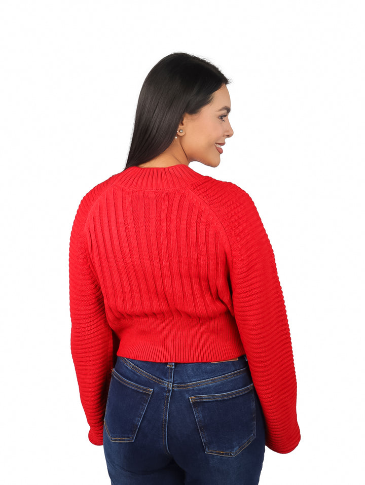 Mujer vistiendo un suéter rojo de tejido acanalado con mangas anchas y pantalones azules.