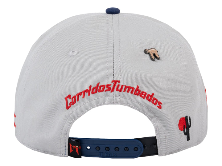 Gorra snapback gris con visera azul marino y detalles en rojo.