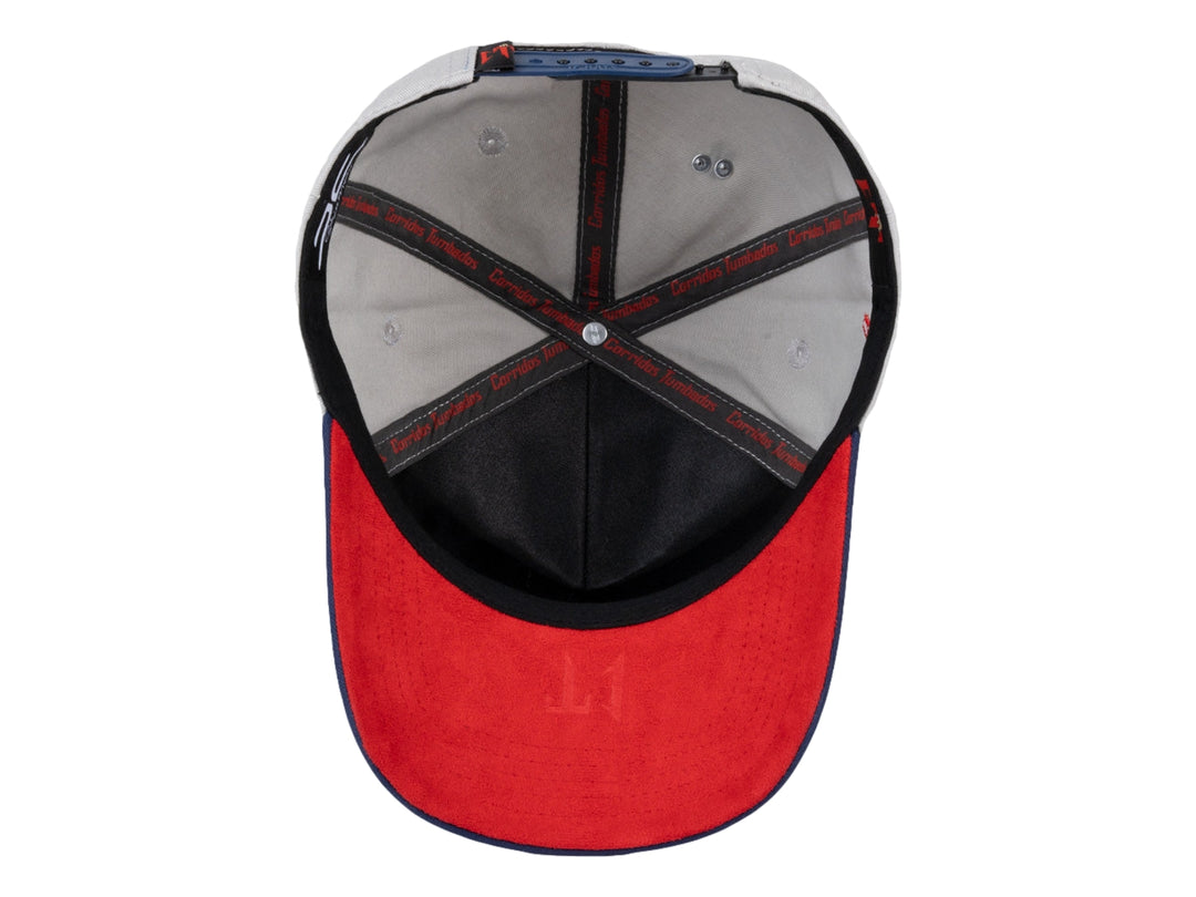 Gorra snapback gris con visera azul marino y detalles en rojo.