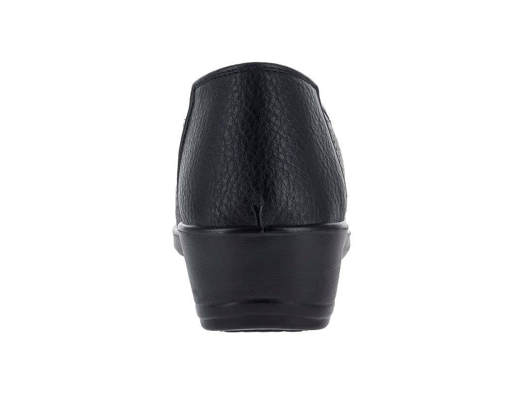 Zapato plano negro con textura perforada, detalle de moño dorado y suela ligera.
