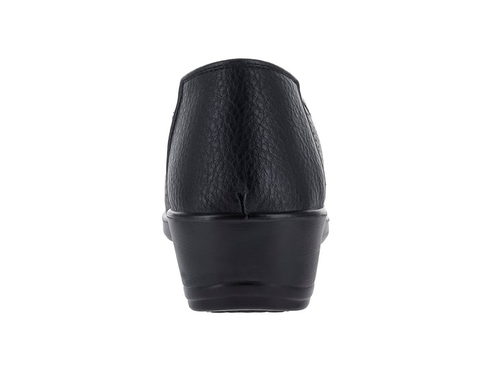 Zapato plano negro con textura perforada, detalle de moño dorado y suela ligera.